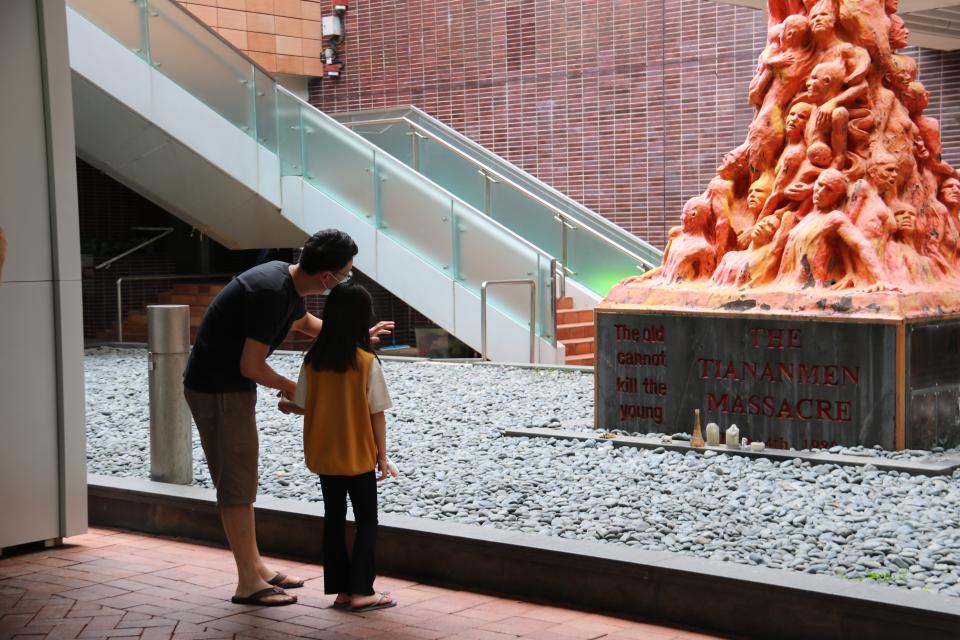 A man points at the Pillar of Shame sculpture through a glass window to a young girl.