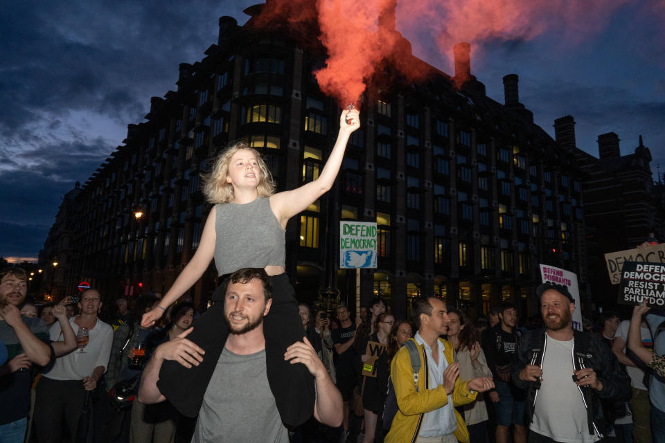 A woman is seen with a flare on westminster bridge outside the houses of parliament where hundreds of people are seen protesting against Boris Johnson