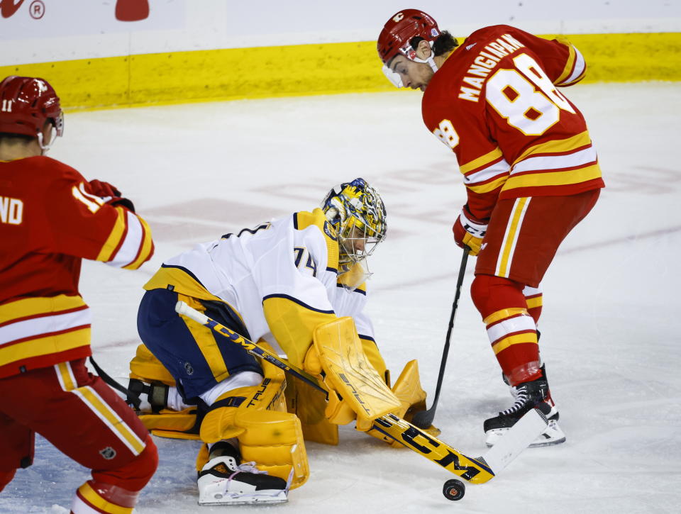 Nashville Predators goalie Juuse Saros, left, swats the puck away from Calgary Flames forward Andrew Mangiapane during the first period of an NHL hockey game in Calgary, Alberta, Monday, April 10, 2023. (Jeff McIntosh/The Canadian Press via AP)