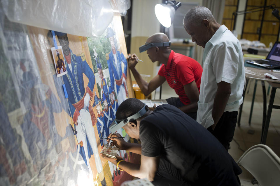 In this May 28, 2019 photo, Haitian artist Ernst Jeudy, left, helps to restore a painting by Haitian artist Edouard Duval Carrie, along with Franck Louissaint, center, Marc Gerard Estime, at the Musée d'Art du Collège Saint Pierre, in Port-au-Prince, Haiti. "This means a lot to me because it's the restoration of a very rich heritage," he said. "It's great to be able to work and transmit this to future generations." Jeudy said. (AP Photo/Dieu Nalio Chery)