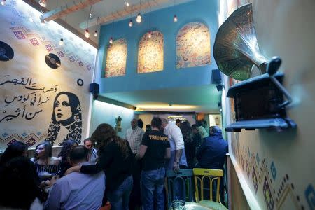 People sit at a newly opened pub near a stencil of Lebanese singer Fayrouz in Damascus, Syria, March 24, 2016. REUTERS/Omar Sanadiki