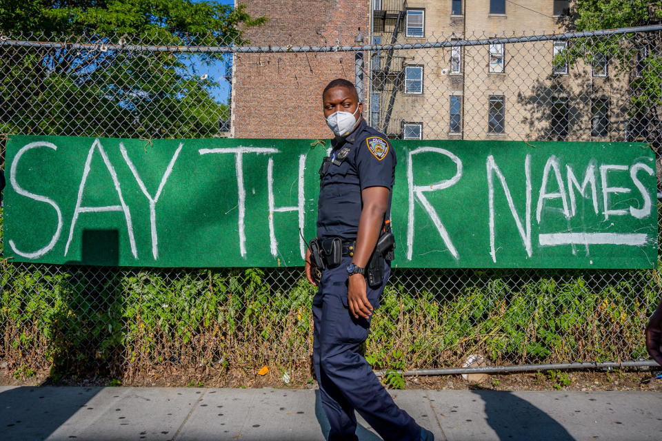 <i>An NYPD officer walks by a banner reading "Say Their Names" on June 1 in Brooklyn, New York. </i>