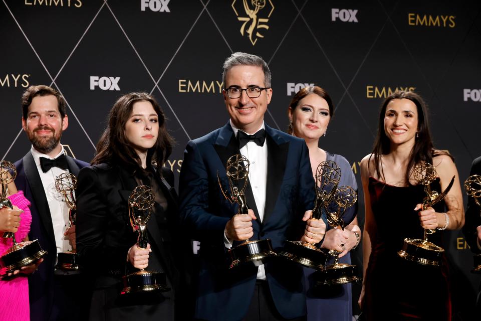 john oliver poses with writers for last week tonight with john oliver at the emmys. all of them are in formal wear and holding golden emmy statuettes, oliver has one in each hand