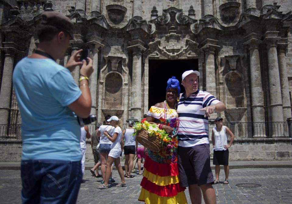 In this picture taken Sept 11, 2012, Russian tourists take pictures of themselves with a Cuban woman dressed in a traditional outfit who takes tips for posing for photos outside the Cathedral in Havana, Cuba. When the Obama administration loosened travel restrictions to Cuba, the thought was that Americans were going to pour into the island on legal cultural exchanges. But several U.S. travel operators complain that, just over a year after the U.S. re-instituted so-called people-to-people exchanges to Cuba, applications to renew their licenses are languishing, forcing cancellations, layoffs and the loss of millions of dollars in revenue. (AP Photo/Ramon Espinosa)