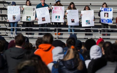 Students from Washington-Lee High School hold up posters, with pictures of those killed in the Parkland school shooting, during a walk out in Arlington, Virginia on March 14, 2018 - Credit:  AFP