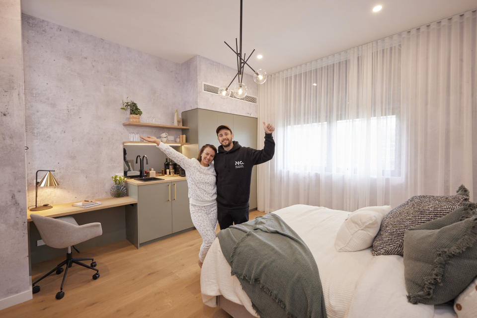 Kristy and Brett pose with their arms in the air in the centre of the bedroom 