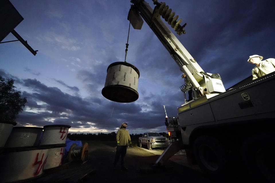 A worker stands by to guide a spool of electrical wire being loaded onto his truck before heading out at dawn, inside a tent city for electrical workers in Amelia, La., Friday, Sept. 17, 2021. When Hurricane Ida was brewing in the Gulf of Mexico, the grass was chest high and the warehouse empty at this lot in southeastern Louisiana. Within days, electric officials transformed it into a bustling “tent city” with enormous, air-conditioned tents for workers, a gravel parking lot for bucket trucks and a station to resupply crews restoring power to the region. (AP Photo/Gerald Herbert)