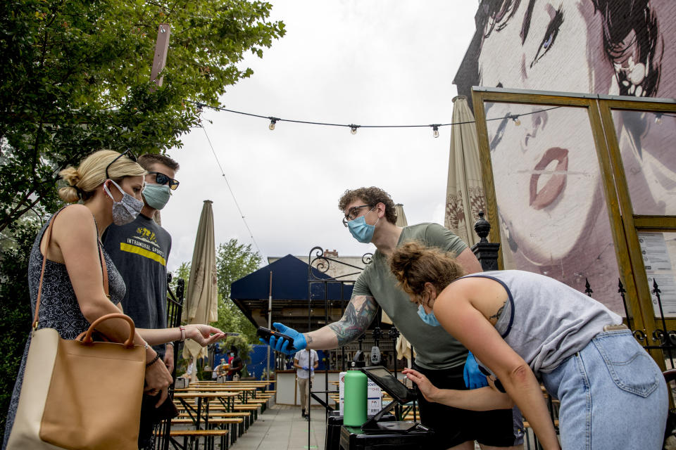 A large Elizabeth Taylor mural is visible behind Steven Scammacca, center right, as he checks IDs and Amy Symonds as she works at Dacha Beer Garden which has opened in the Shaw neighborhood in Washington, Friday, May 29, 2020, as the District of Columbia gradually loosens stay-at-home rules that have been in place since March 25 because of the pandemic and allows restaurants to resume outdoor dining. (AP Photo/Andrew Harnik)