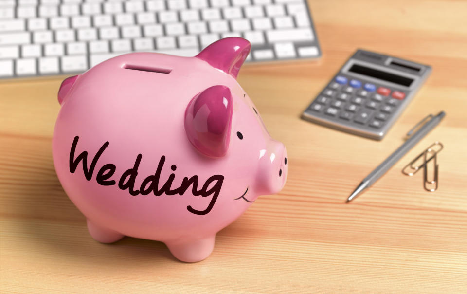 A piggy bank with the word "Wedding" written on the side next to a calculator and pen