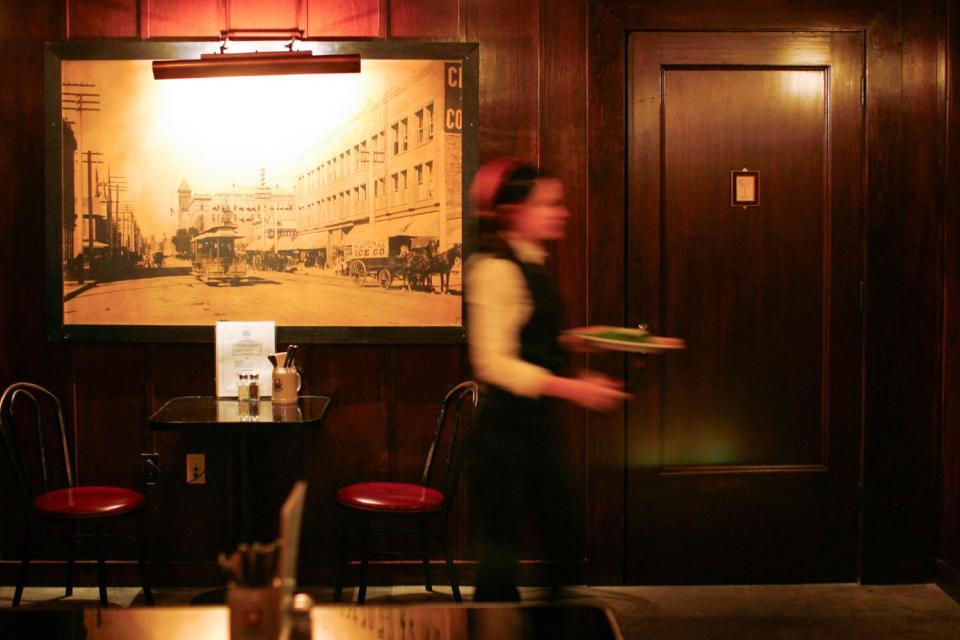 A server walking in front of a wall with a black and white photo of a city and a plain door.