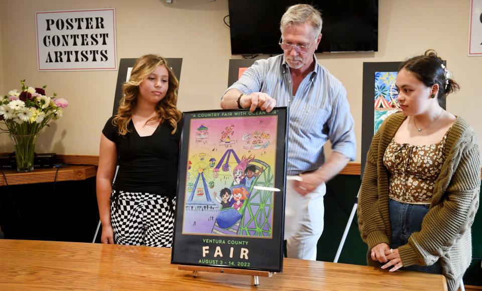 Vita Jolie Vazquez, 12, of Fillmore, left, stands next to the 2022 Ventura County Fair poster created with her artwork, held up by the fair's marketing manager, James Lockwood, on Friday. Amy Midence, 17, of Oxnard, right, won second place.
