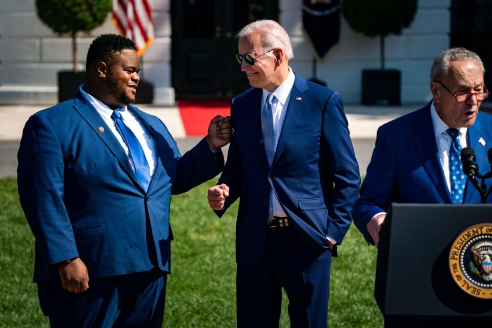 Two people face each other next to a person speaking at a lectern outdoors.