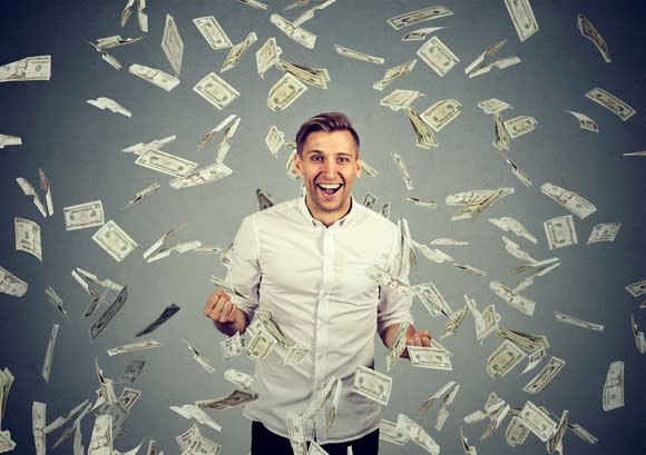 A young man in a dress shirt surrounded by falling paper currency.