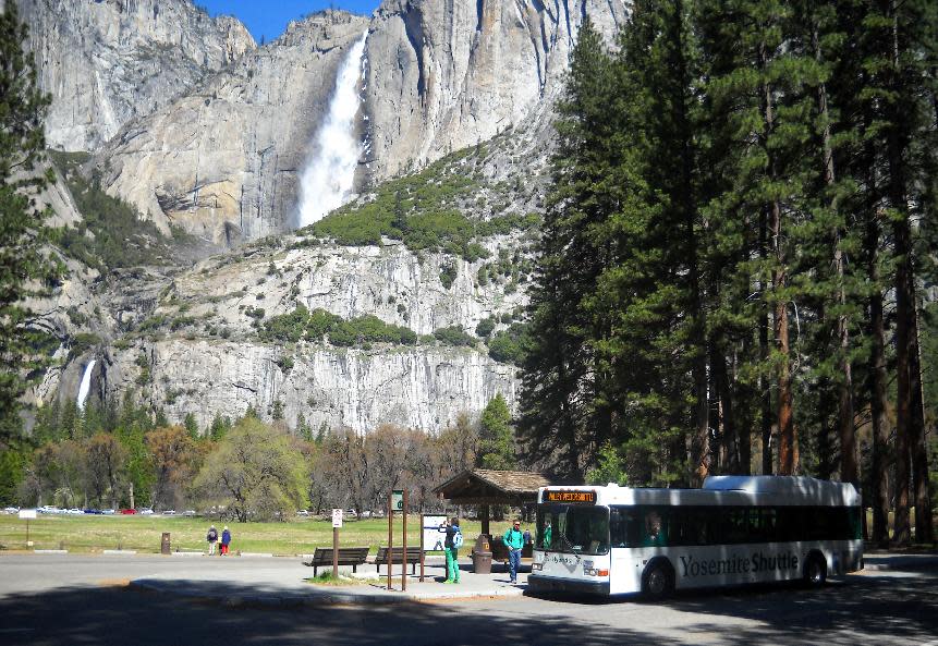 This April 2013 photo shows the free shuttle bus at Yosemite National Park picking up passengers at Sentinel Bridge, with Yosemite Falls in the background. No matter how visitors travel around the park, it's impossible not to see something beautiful. (AP Photo/Kathy Matheson)