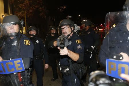 A police officer aims his weapon towards protesters during a march against the New York City grand jury decision to not indict in the death of Eric Garner in Berkeley, California December 8, 2014. REUTERS/Stephen Lam