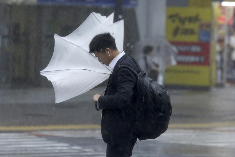 A man struggles with his umbrella against strong wind at a crossing in Shibuya district, Tokyo Saturday, Oct. 12, 2019. Tokyo and surrounding areas braced for a powerful typhoon forecast as the worst in six decades, with streets and trains stations unusually quiet Saturday as rain poured over the city. (AP Photo/Kiichiro Sato)