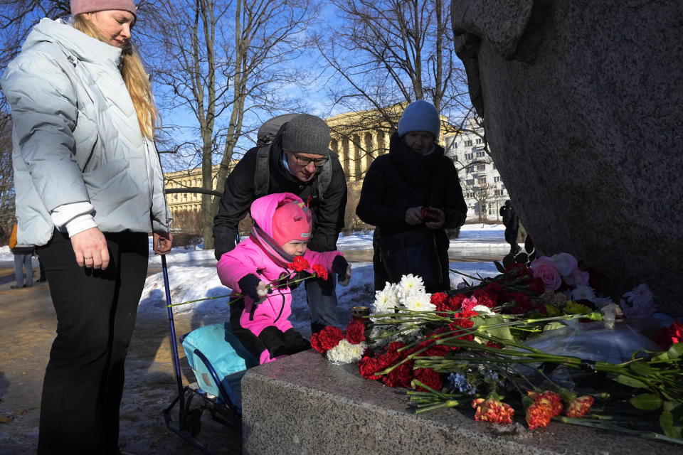 A family pay tribute to Alexei Navalny at the monument, a large boulder from the Solovetsky islands, where the first camp of the Gulag political prison system was established in St. Petersburg, Russia, Sunday, Feb. 18, 2024. Russians across the vast country streamed to ad-hoc memorials with flowers and candles to pay tribute to Alexei Navalny, the most famous Russian opposition leader and the Kremlin's fiercest critic. Russian officials reported that Navalny, 47, died in prison on Friday. (AP Photo/Dmitri Lovetsky)