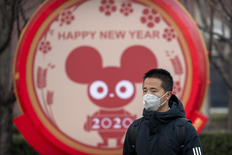 FILE - In this Jan. 22, 2020 photo, a man wears a face mask as he walks past a display for the upcoming Lunar New Year, the Year of the Rat, in Beijing, Wednesday, Jan. 22, 2020. A virus that has killed more than two dozen people and sickened hundreds more has all but shut down China's biggest holiday of the year, the Lunar New Year. Instead of family reunions or sightseeing trips, many of the country's 1.4-billion people are hunkering down as the country scrambles to prevent the illness from spreading further. (AP Photo/Mark Schiefelbein, File)