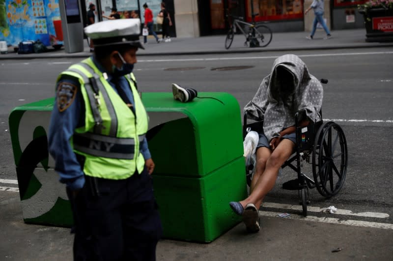 A man sits in a wheelchair as a NYPD traffic officer passes by near Times Square in New York City