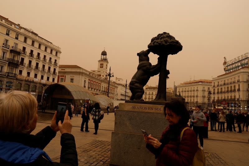 FILE PHOTO: Tourists take pictures of Puerta del Sol square as storm Celia blew sand from the Sahara desert over Madrid