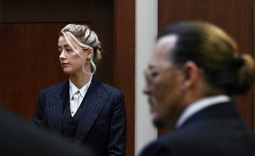 In a courtroom, a woman is in focus in the background while a man appears blurred in profile in the foreground