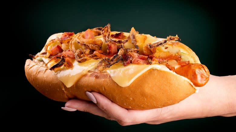 hand with bacon hot dog