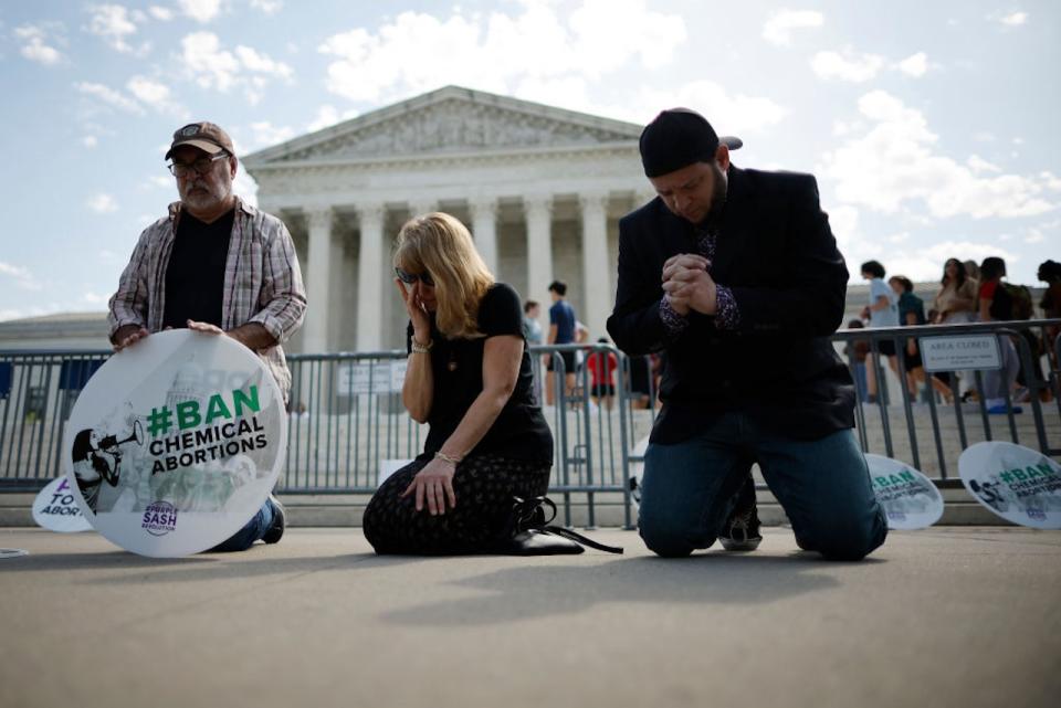 People kneeling in prayer in front of the U.S. Supreme Court building.