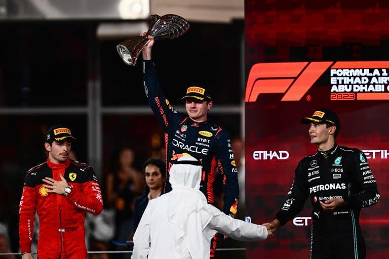 Red Bull Racing's Dutch driver Max Verstappen (C) raises the winners' trophy as he stands on the podium with Ferrari's Monegasque driver Charles Leclerc (L) and Mercedes' British driver George Russell after the Abu Dhabi Formula One Grand Prix at the Yas Marina Circuit in the Emirati city on November 26, 2023. (Photo by Jewel SAMAD / AFP)