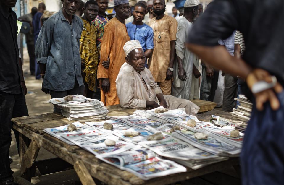 Nigerians gather around to look at the day's front pages at a newspaper stand in Kano, in northern Nigeria Sunday, Feb. 24, 2019. Vote counting continued Sunday as Nigerians awaited the outcome of a presidential poll seen as a tight race between the president and a former vice president. (AP Photo/Ben Curtis)