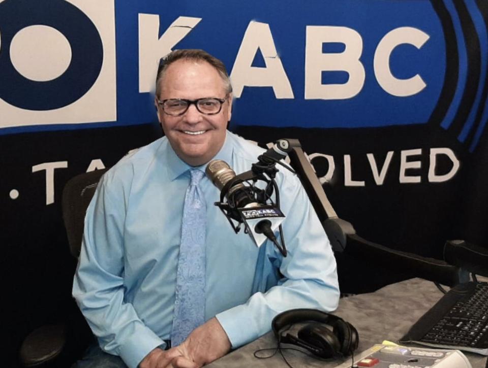 A man in glasses sits behind a microphone in a radio studio