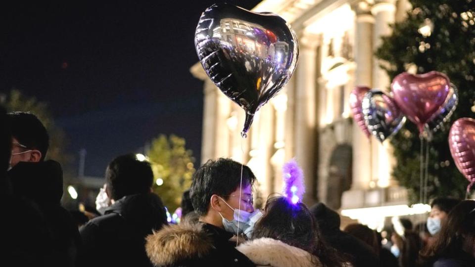 A couple kissing in the street holding a balloon