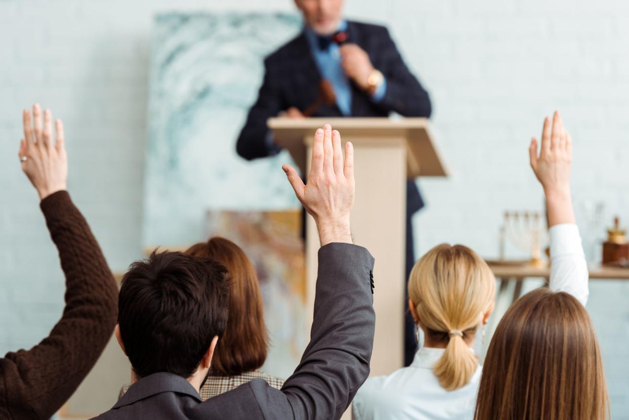 back view of buyers raising hands to auctioneer during auction