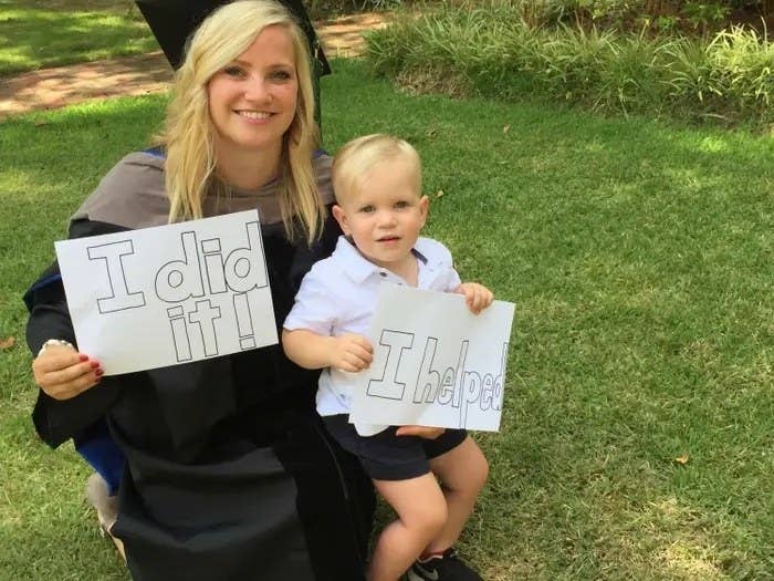 The author at her graduation with her son; she's holding up an "I did it!" sign and he's holding an "I helped" sign