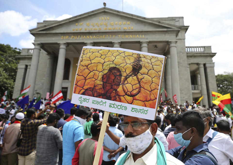 A protester wears a face mask as a precaution against the coronavirus as he holds a placard during a protest against a pair of controversial agriculture bills in Bengaluru, India, Monday, Sept. 28, 2020. India's confirmed coronavirus tally has reached 6 million cases, keeping the country second to the United States in number of reported cases since the pandemic began. (AP Photo/Aijaz Rahi)