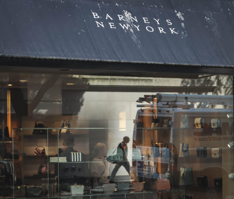 FILE - In this July 16, 2019, file photo a pedestrian reflect in a store window at Barneys department store in New York. Barneys New York, which opened its 10-story Madison Avenue store in 1993, became a cultural icon in luxury shopping but now risks closure. High rents and a dramatic shift toward online shopping are pressuring it to evaluate restructuring options, including possible bankruptcy, according to a source close to the matter who asked to remain anonymous because the discussions are confidential. (AP Photo/Bebeto Matthews, File)