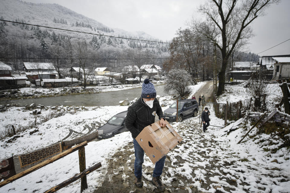 Valeriu Nicolae carries a box containing basic food, hygiene and medical products on a muddy slope in Nucsoara, Romania, Saturday, Jan. 9, 2021. Nicolae and his team visited villages at the foot of the Carpathian mountains, northwest of Bucharest, to deliver aid. The rights activist has earned praise for his tireless campaign to change for the better the lives of the Balkan country’s poorest and underprivileged residents, particularly the children. (AP Photo/Andreea Alexandru)