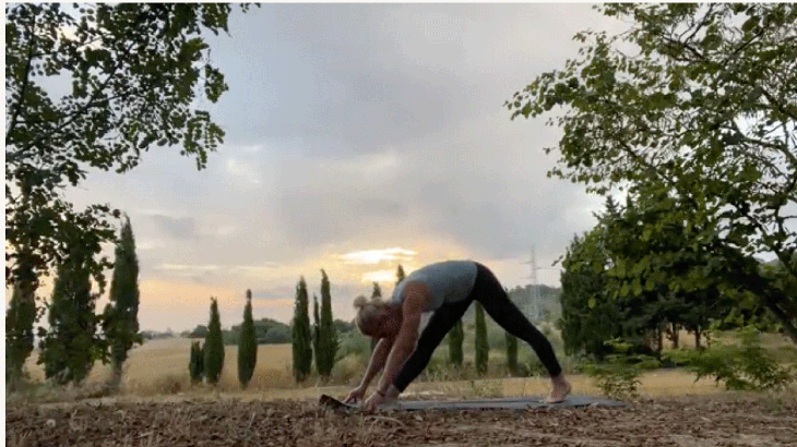 Woman practicing yoga outside early morning with her hands on the mat stretching her hamstrings