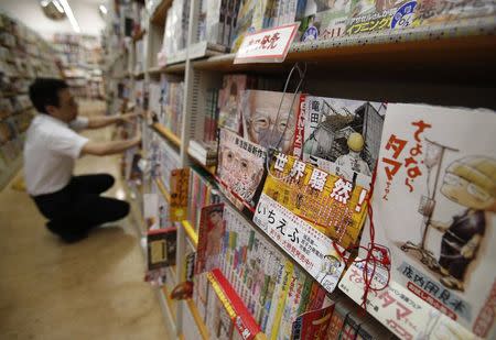 A Japanese Manga "Ichi Efu" (2nd R), which centres on workers at the Fukushima Daiichi nuclear plant, is seen on a bookshelf as a staff adjusts manga comics at a bookstore in Tokyo June 23, 2014. REUTERS/Yuya Shino