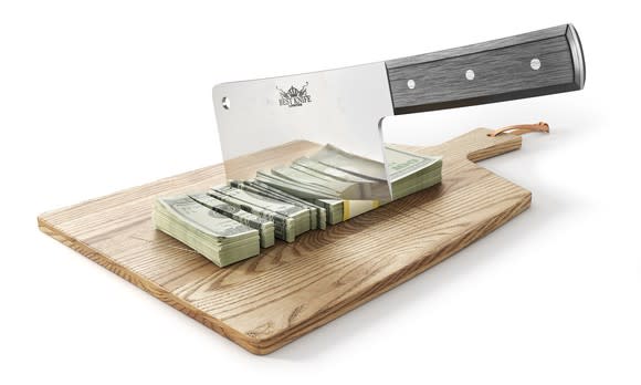 A cleaver cutting through a stack of money on a chopping board.