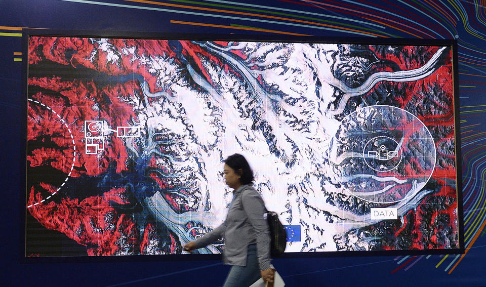 In this Dec. 11, 2018 photo a participant in U.N. climate conference walks by a photo of a satellite in Katowice, Poland. A growing fleet of satellites is monitoring man-made greenhouse gas emissions from space, spurred by the need to track down major sources of climate changing gases such as methane and carbon dioxide. (AP Photo/Czarek Sokolowski)