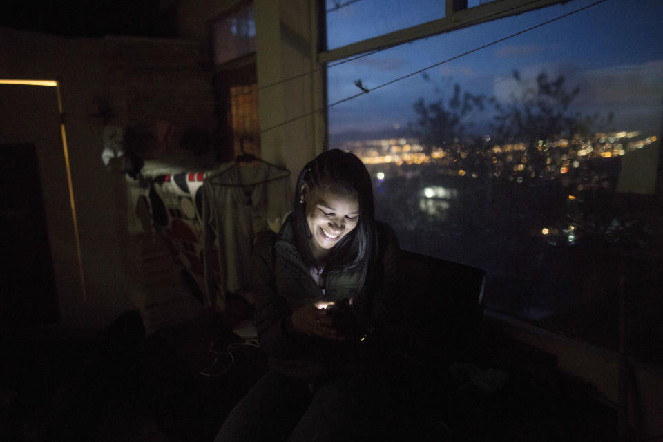 In this In this Dec. 11, 2018 photo, Venezuelan Emili Espinoza smiles during a video call with her children, in the room she shares with other migrants in Bogota, Colombia. Like other migrants, Venezuelan families are likely to try to reunite as quickly as possible, a trend Colombian authorities believe is already underway. Officials project that family reunifications will result in even higher numbers of Venezuelans living abroad. (AP Photo/Ivan Valencia)