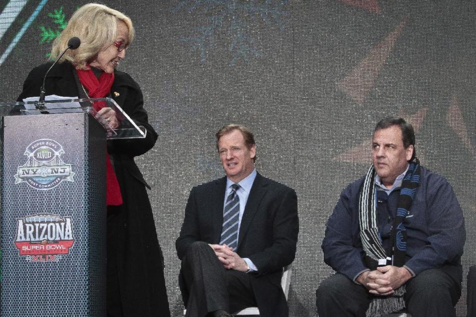 NFL Commissioner Roger Goodell, center, and New Jersey Gov. Chris Christie, right, display different reactions as Arizona Gov. Jan Brewer, left, speaks during a ceremony to pass official hosting duties of next year's Super Bowl to Arizona, Saturday Feb. 1, 2014 in New York. (AP Photo/Bebeto Matthews)