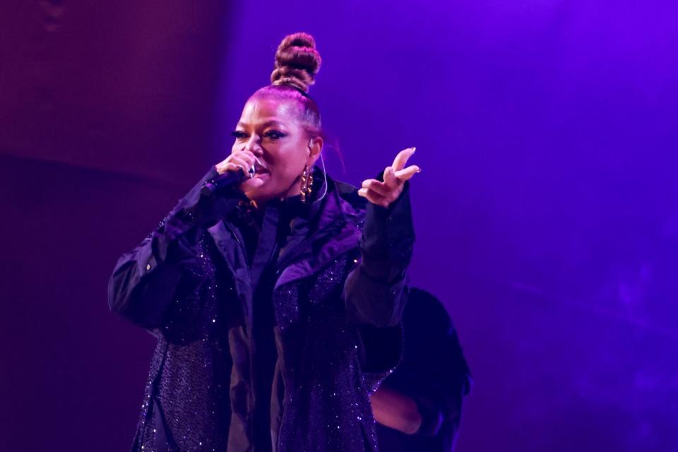 A woman with brown hair in a bun wears a sparkly black coat holds a microphone