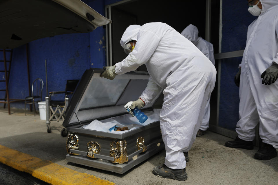 A worker wearing protective gear sprays disinfectant solution inside the coffin of a person who died from suspected COVID-19, as the body arrives at the crematorium at Xilotepec Cemetery in Xochimilco, Mexico City, Monday, July 27, 2020. (AP Photo/Rebecca Blackwell)