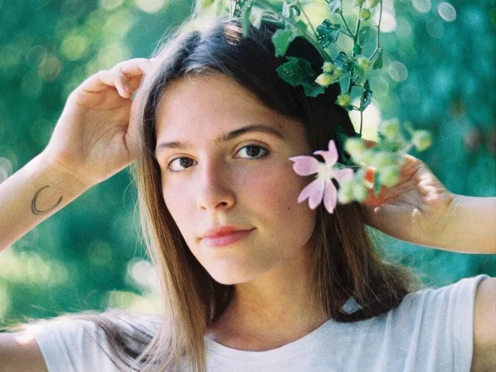 Oleksandra "Sasha" Kuvshynova in head and shoulders portrait. She poses in a white t-shirt with blossoms.