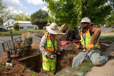 Teichert Construction laborer Israel Moreo (L) and plumber Victor De Anda install a water meter on 21st Street during the city's water meter retrofitting program in Sacramento, April 8, 2015. REUTERS/James Glover III