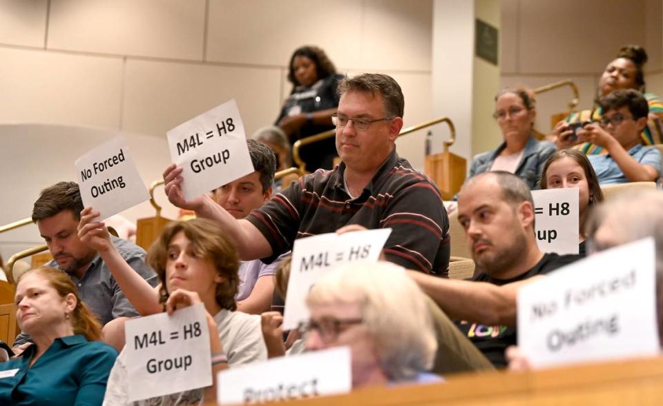 Audience members hold up signs as a speaker addresses the Charlotte Mecklenburg school board on Tuesday, August 22, 2023 at the Charlotte-Mecklenburg County Government Center. CMS is one of the first to pass policies to comply with Senate Bill 49.