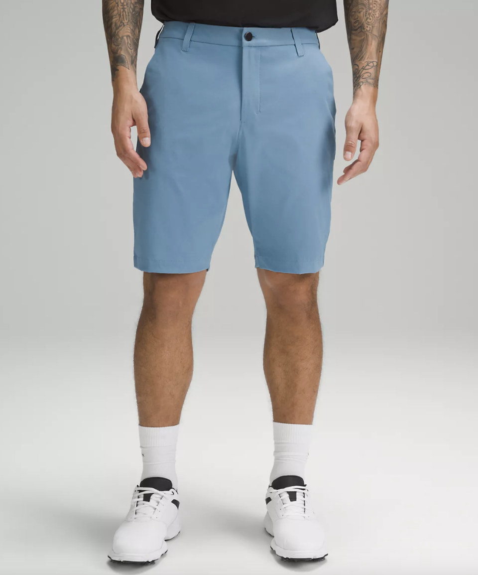 tattooed man wearing white sneakers, white socks and light blue Commission Golf Short 10