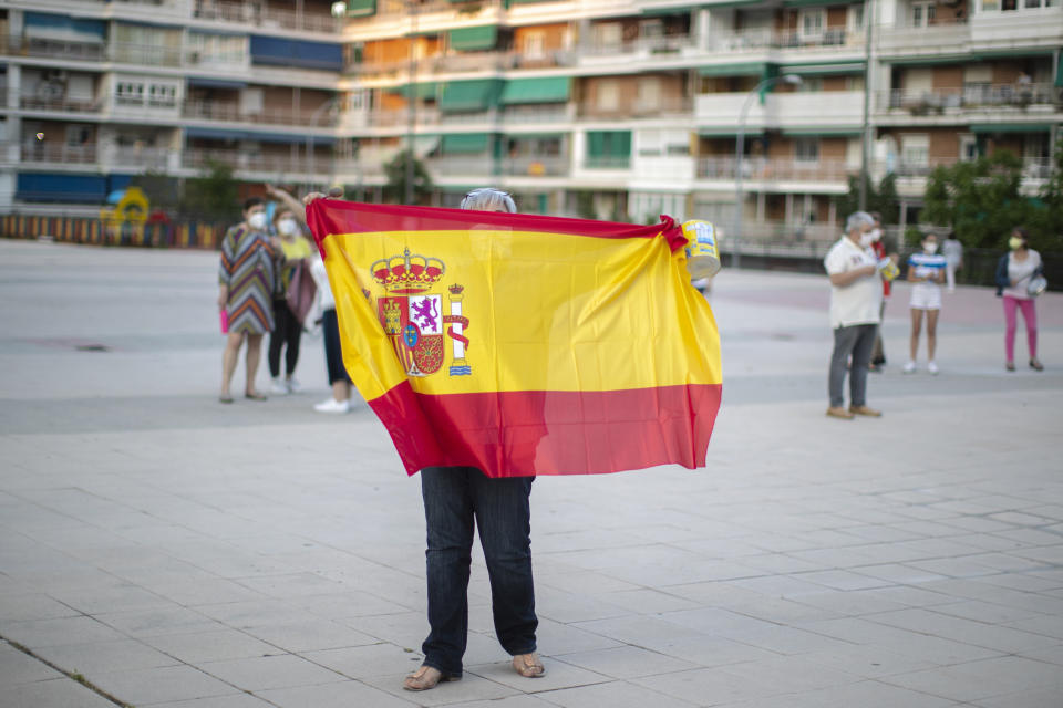 A woman holds a Spanish flag during a protest against the Spanish government amid the lockdown to prevent the spread of coronavirus in Alcorcon, Spain, Friday, May 22, 2020. The Spanish government is allowing Madrid and Barcelona to ease their lockdown measures, which were introduced to fight the coronavirus pandemic. (AP Photo/Manu Fernandez)