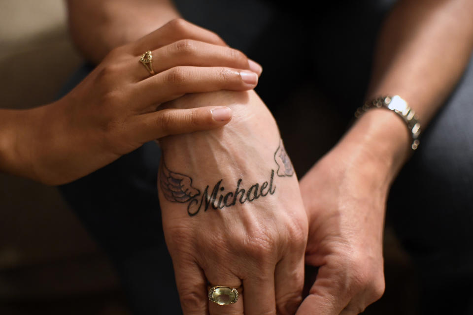 In this Thursday, Jan. 14, 2021 photo, Victoria Mitchell's hand, right, bears a new tattoo with her son Michael Gregory's name as she is touched by Gregory's daughter Mikaiya Gregory Mitchell in Bridgeport, Conn. Connecticut officials are debating a statewide program of voluntary registries of people with mental health problems and disabilities to inform responding officers. Mitchell's son Michael had psychiatric problems and was shot and killed by police in 2020. Mitchell adopted Mikaiya as her daughter after her son's death. (AP Photo/Jessica Hill)